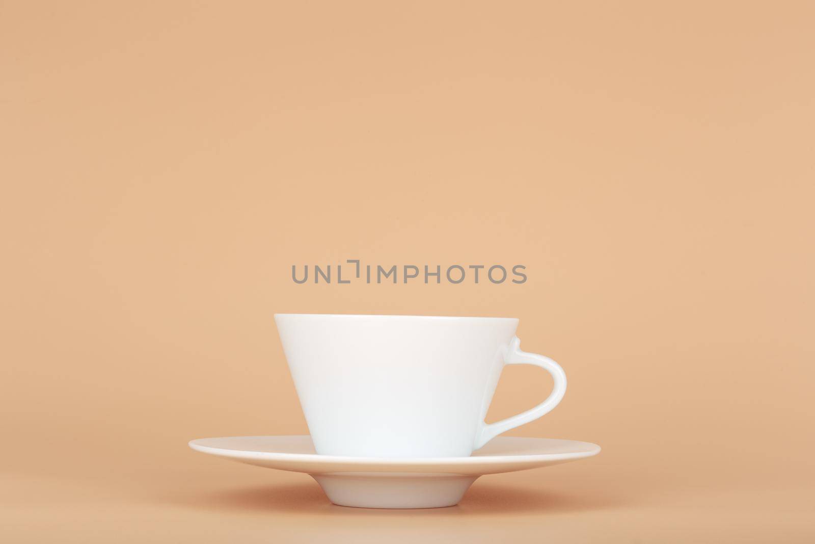 White ceramic coffee cup with saucer against pastel beige background with copy space. Concept of hot drinks, ceramic cups and kitchen utensil