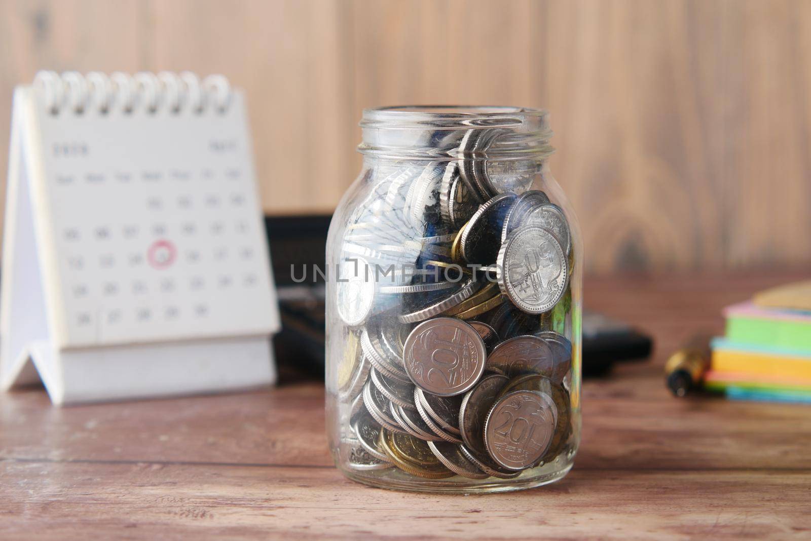 coins in a jar and calendar on table, selective focus