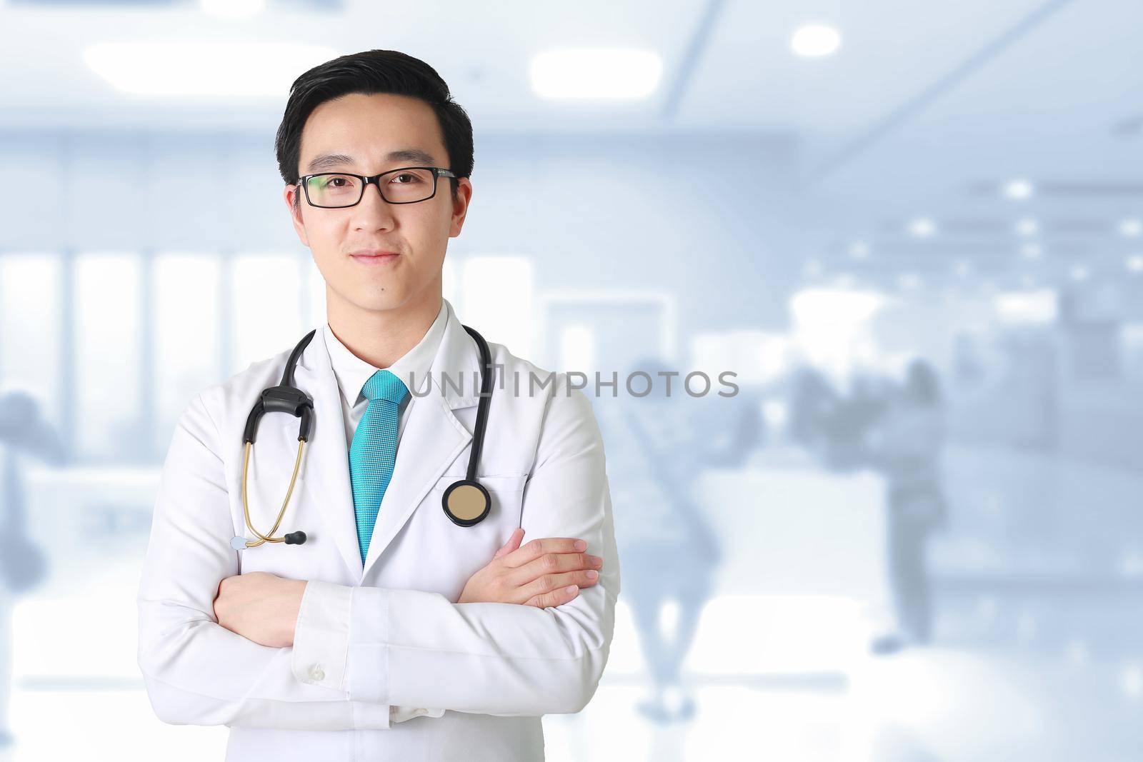 Doctor posing with arms crossed, medical staff working on blurry background.