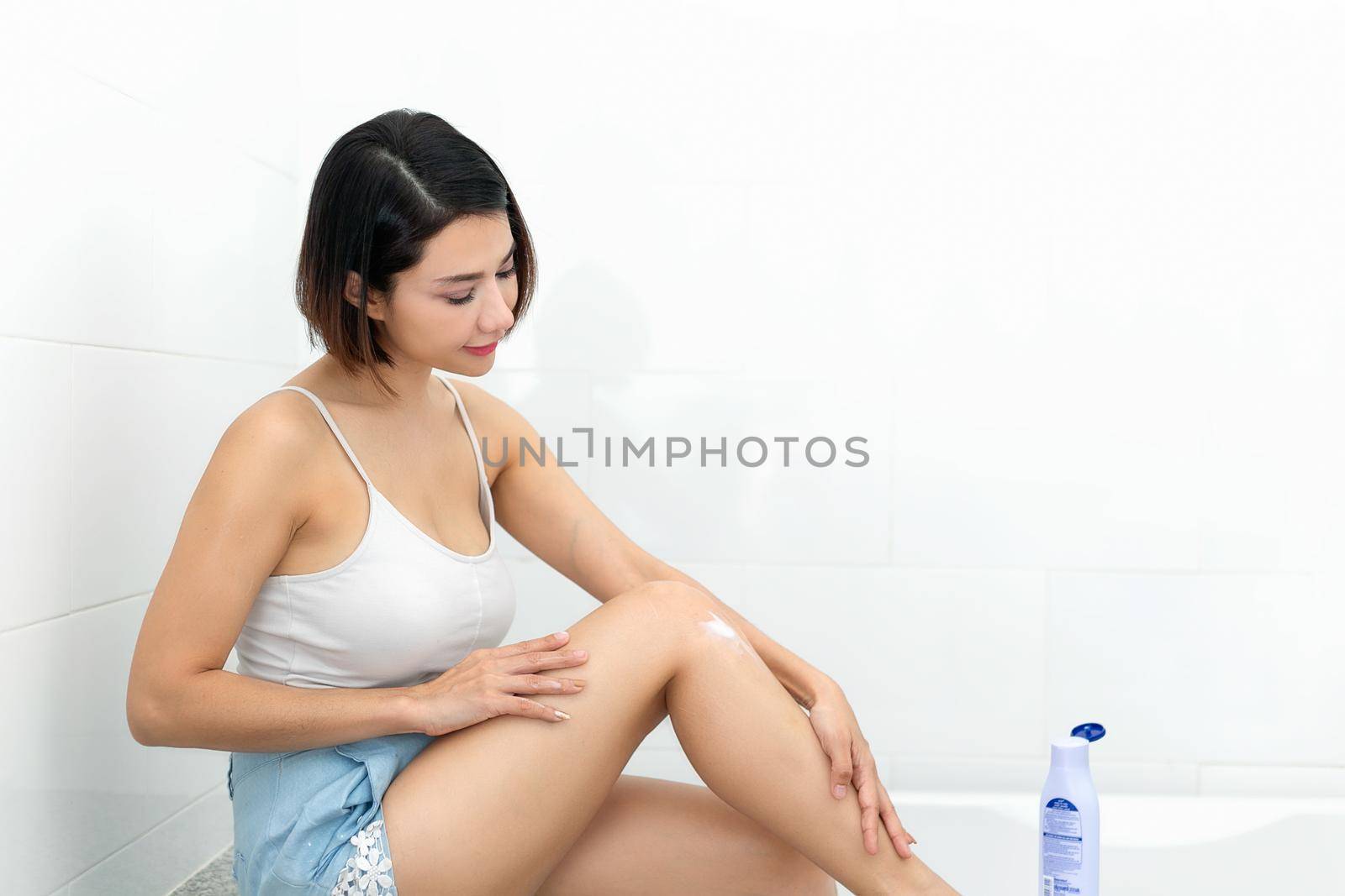 Young woman applying body lotion on her legs. by jayzynism