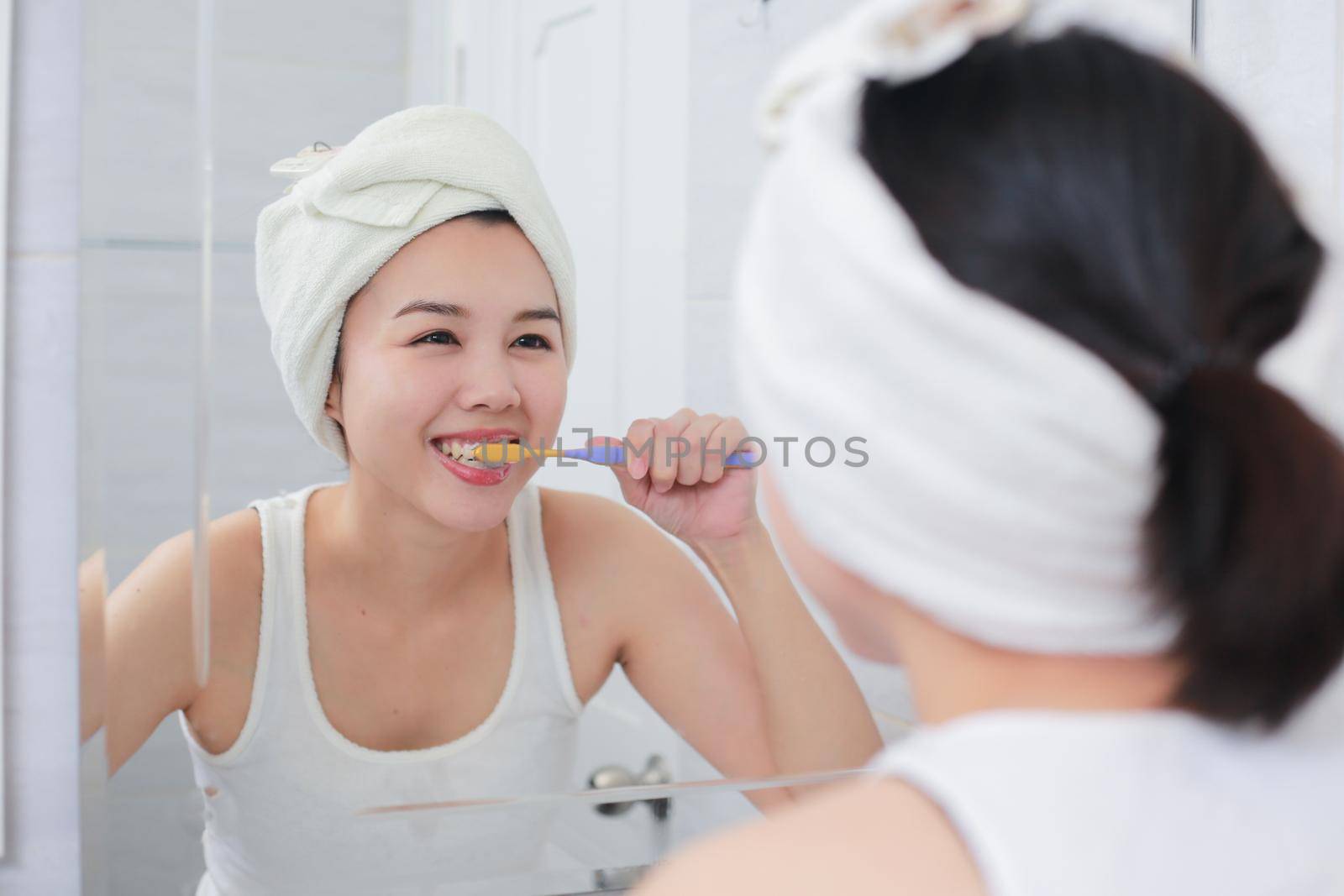 Young asian woman brushing her teeth at the mirror. by jayzynism