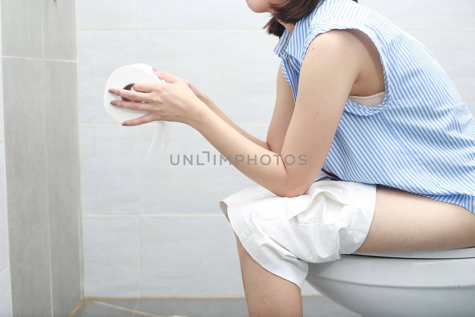 Woman in bath towel sitting on toilet bowl.