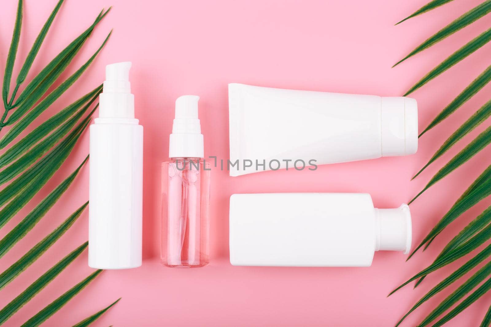 Creative flat lay with cosmetic products for cleaning, moisturizing and exfoliating on pink background with palm leaves. Concept of organic natural beauty products for daily skin care
