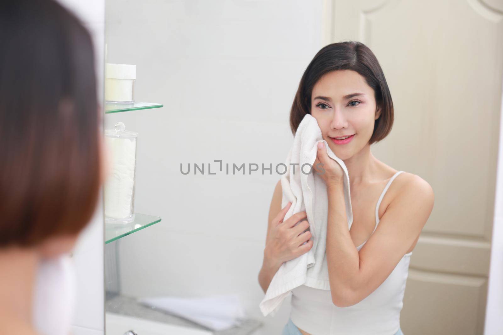 Young asian woman wiping her face with towel in bathroom. by jayzynism