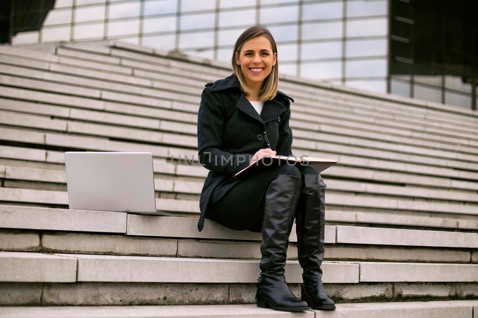 Beautiful businesswoman sitting on the staircase in the city and working.