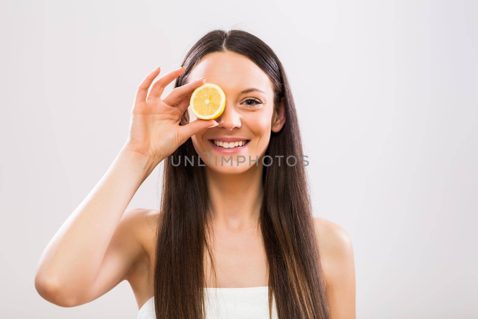 Beautiful woman covering eye with slice of lemon.