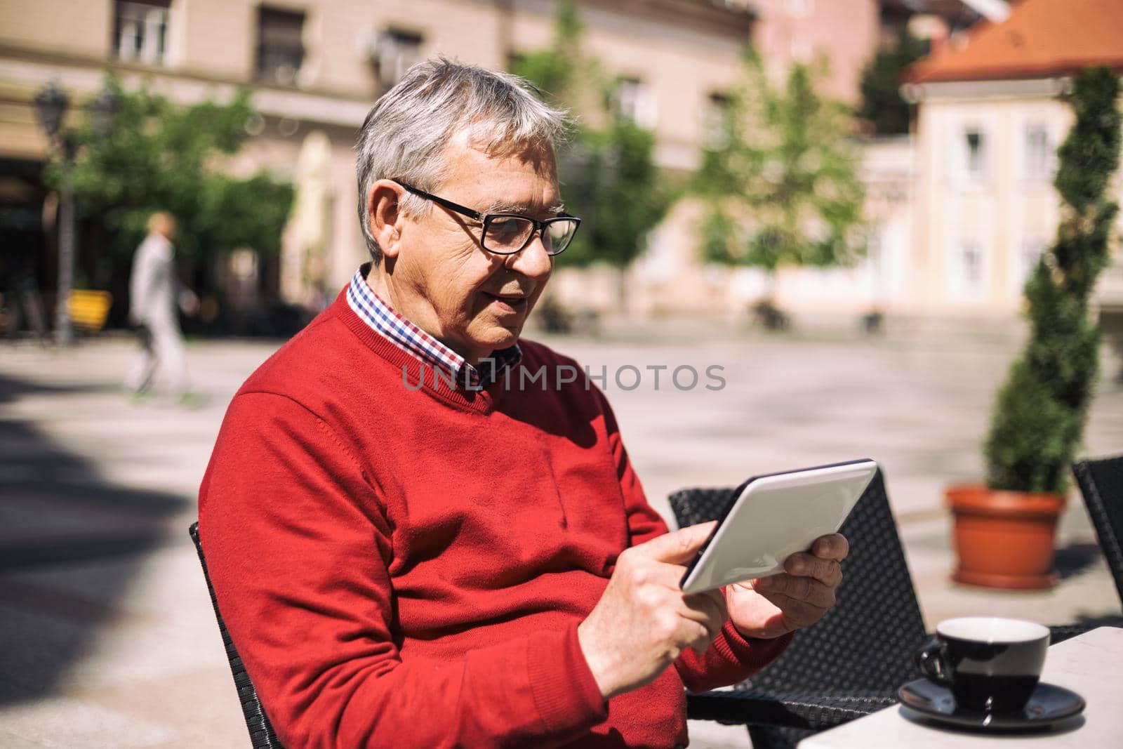 Senior man using digital tablet while drinking coffee at the bar.Image is intentionally toned.