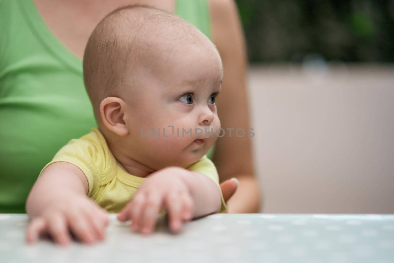 Portrait of cute baby boy enjoys sitting in mother's lap.