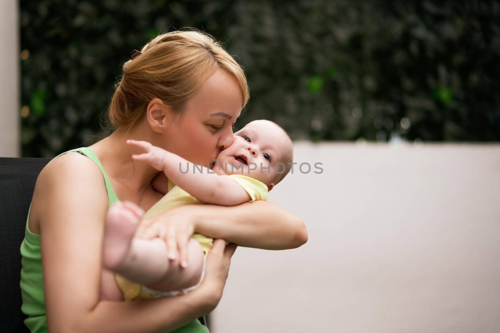 Mother enjoys holding and kissing her little cheerful baby boy.