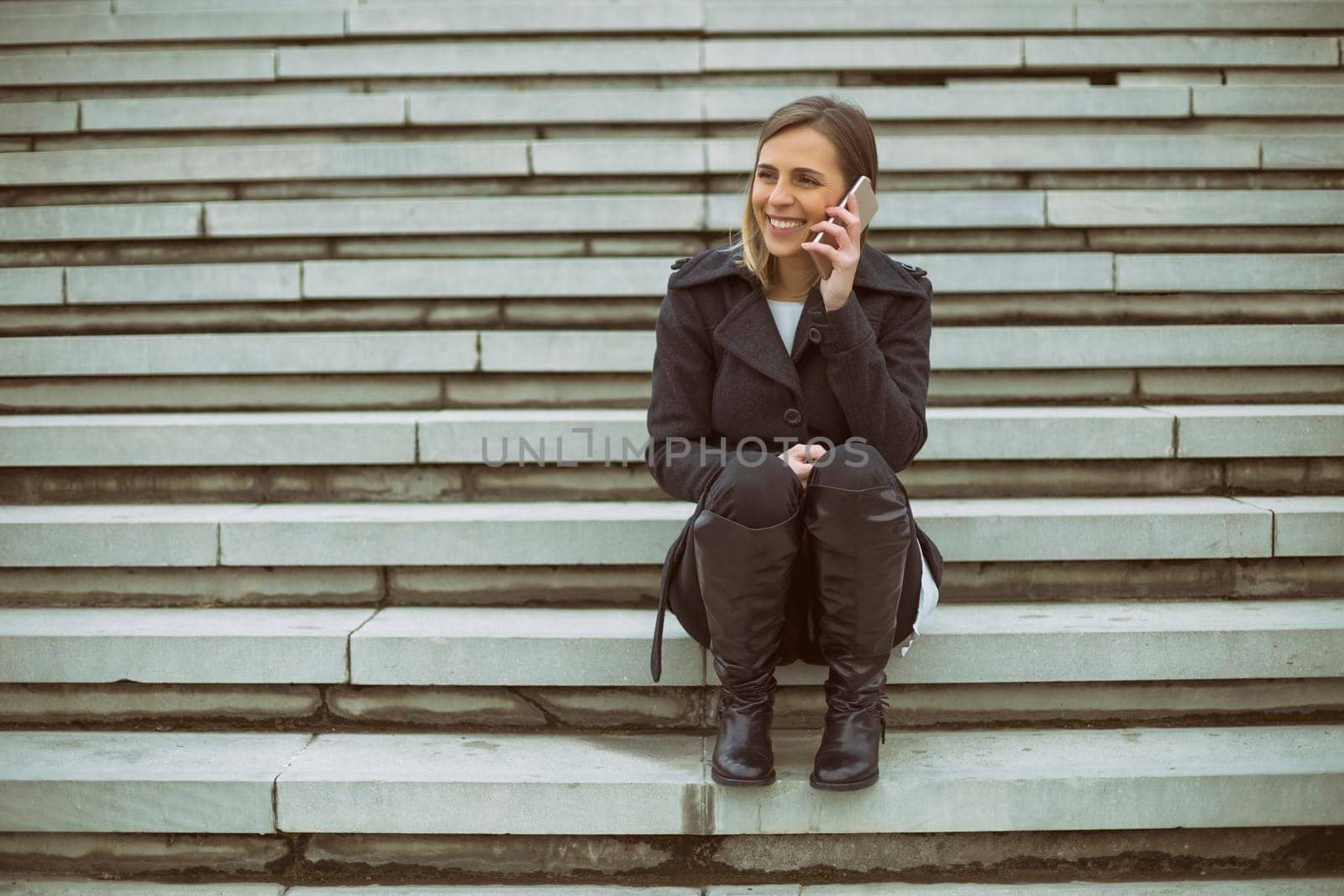 Beautiful businesswoman using phone while sitting on the staircase in the city.