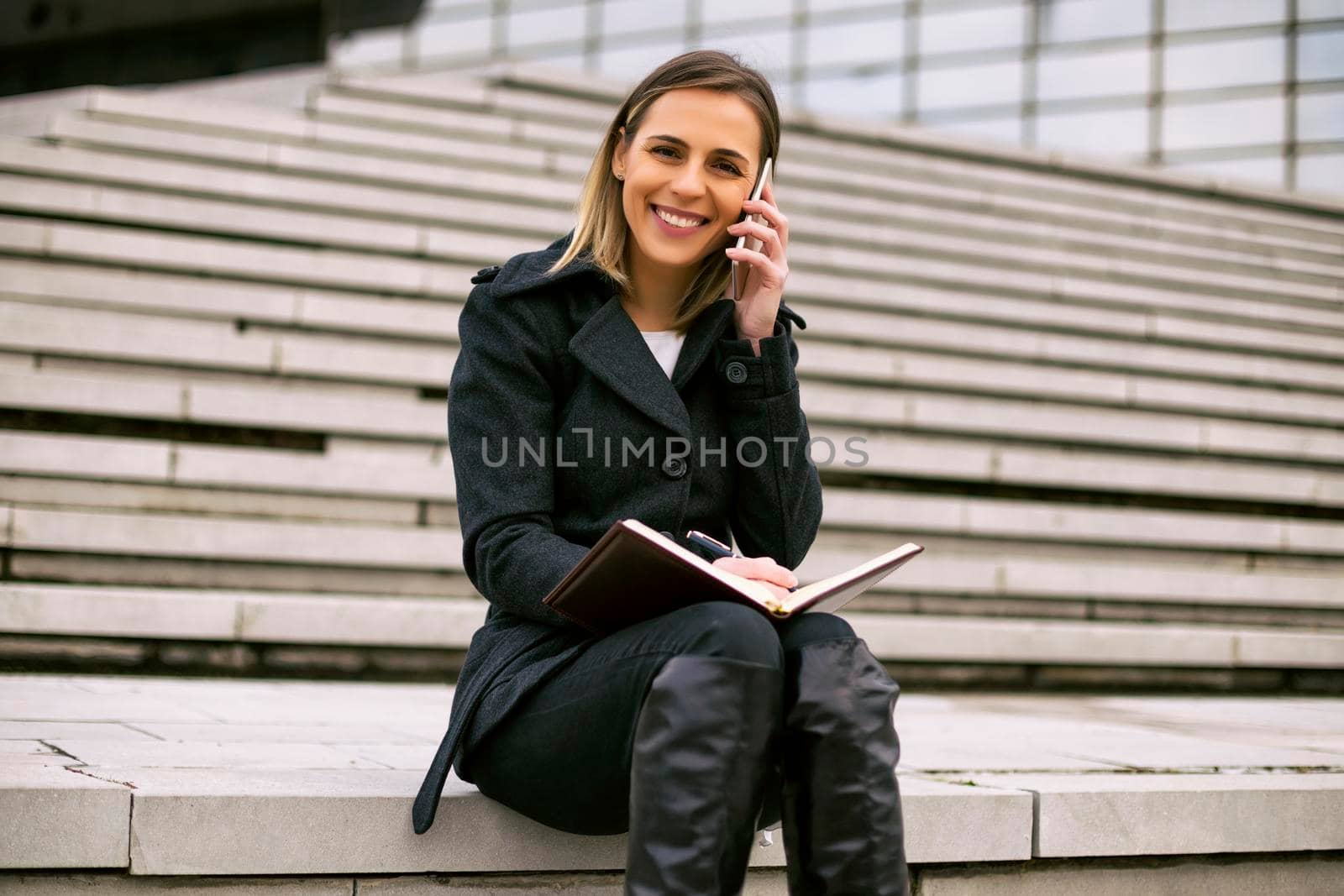 Businesswoman using phone and personal organizer while working by Bazdar