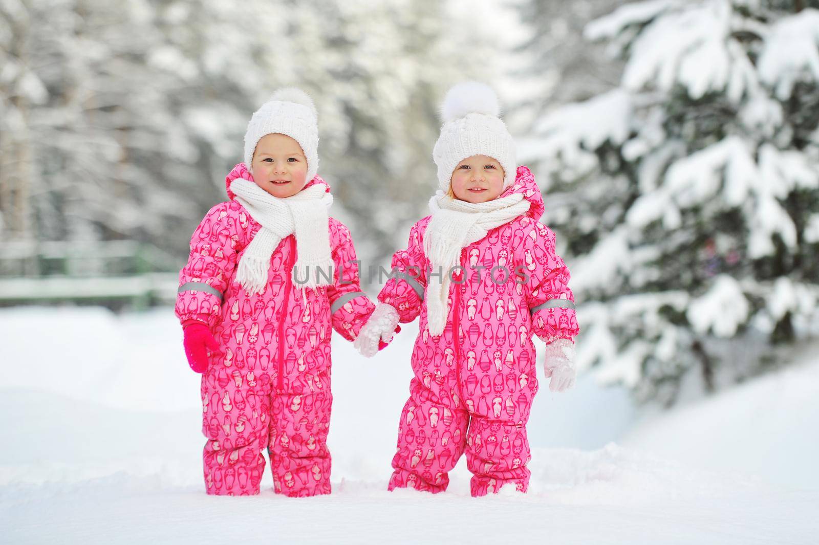 Two little twin girls in red suits stand in a snowy winter forest by Lobachad