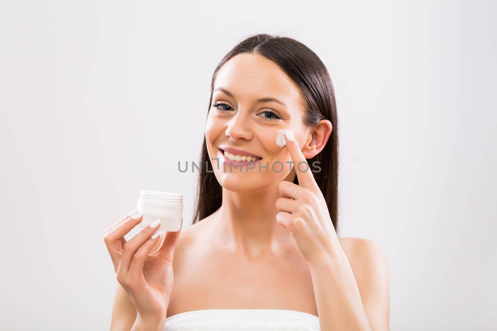 Beautiful woman applying moisturizer on face.