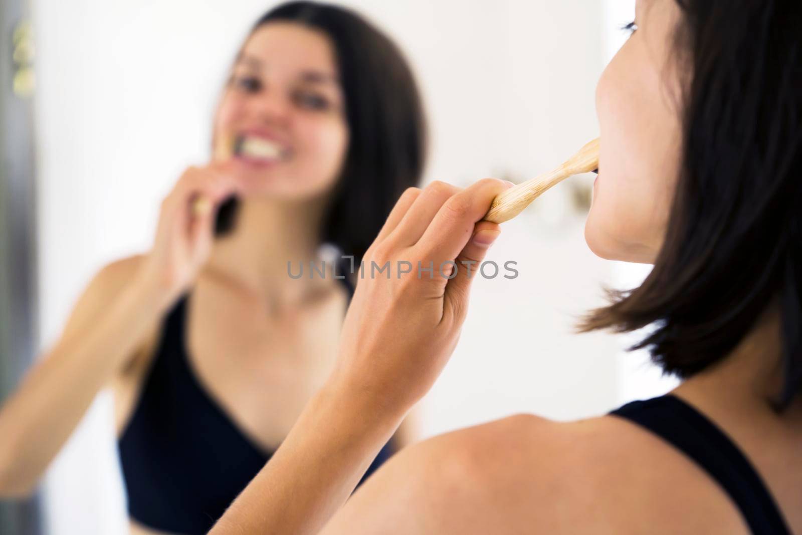 A young girl actively brushes her teeth with a bamboo brush and toothpaste in the bathroom, a woman carefully looks after her teeth.