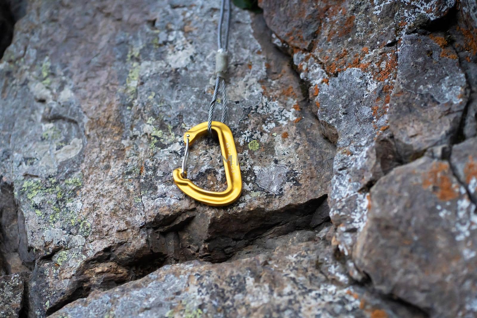 Climbing equipment, the yellow carabiner at the belay station lies on the rock.