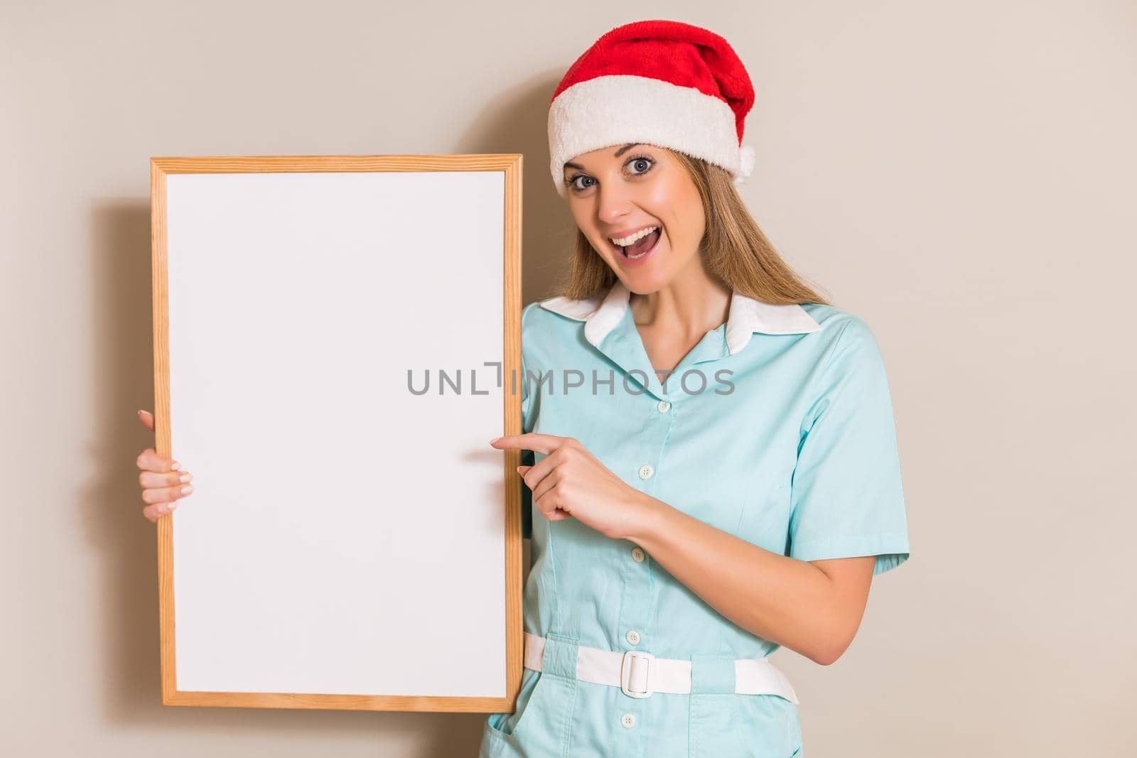 Portrait of nurse with Santa hat pointing at white board.