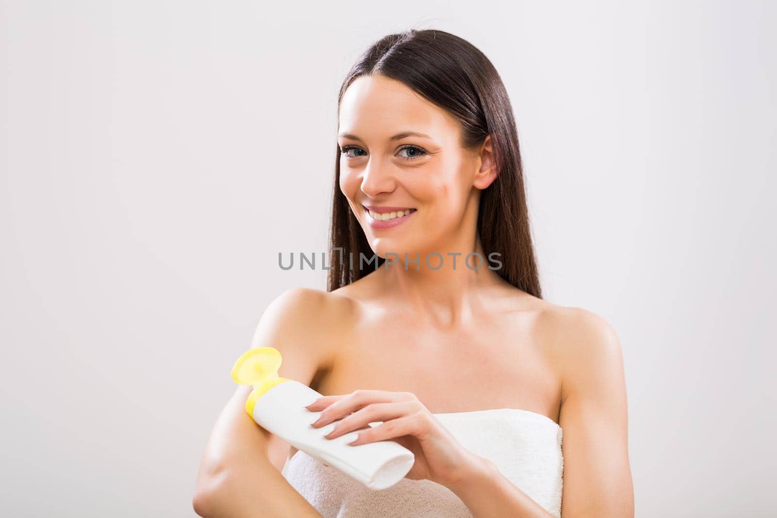 Beautiful woman applying moisturizer on her arm on gray background.