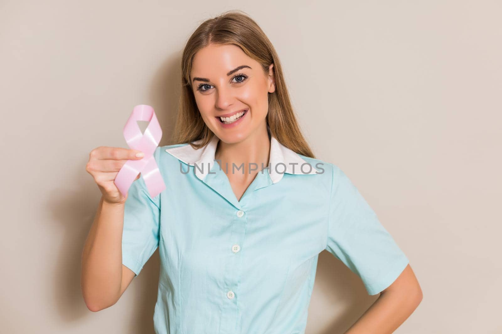 Portrait of beautiful medical nurse showing pink ribbon, breast cancer awareness concept.
