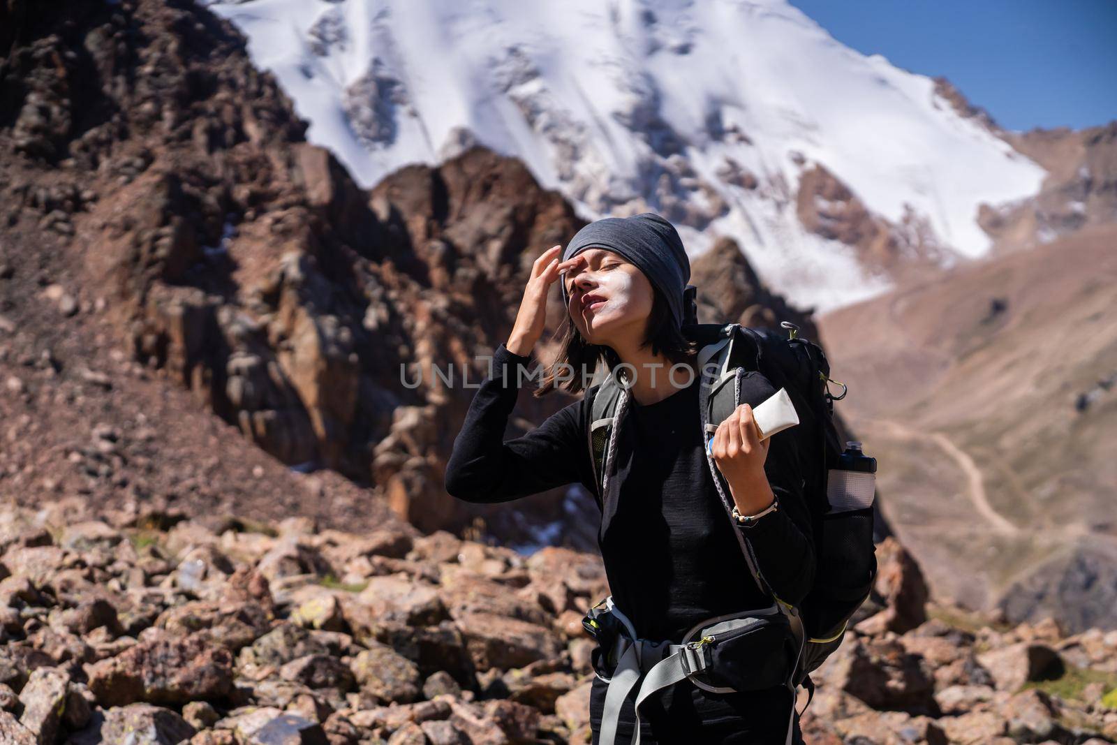 Beautiful young sportive girl applies sunscreen to her hands and face while climbing the mountain, woman takes care of her skin while traveling.
