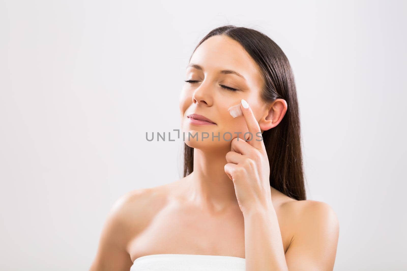 Woman applying moisturizer on face by Bazdar