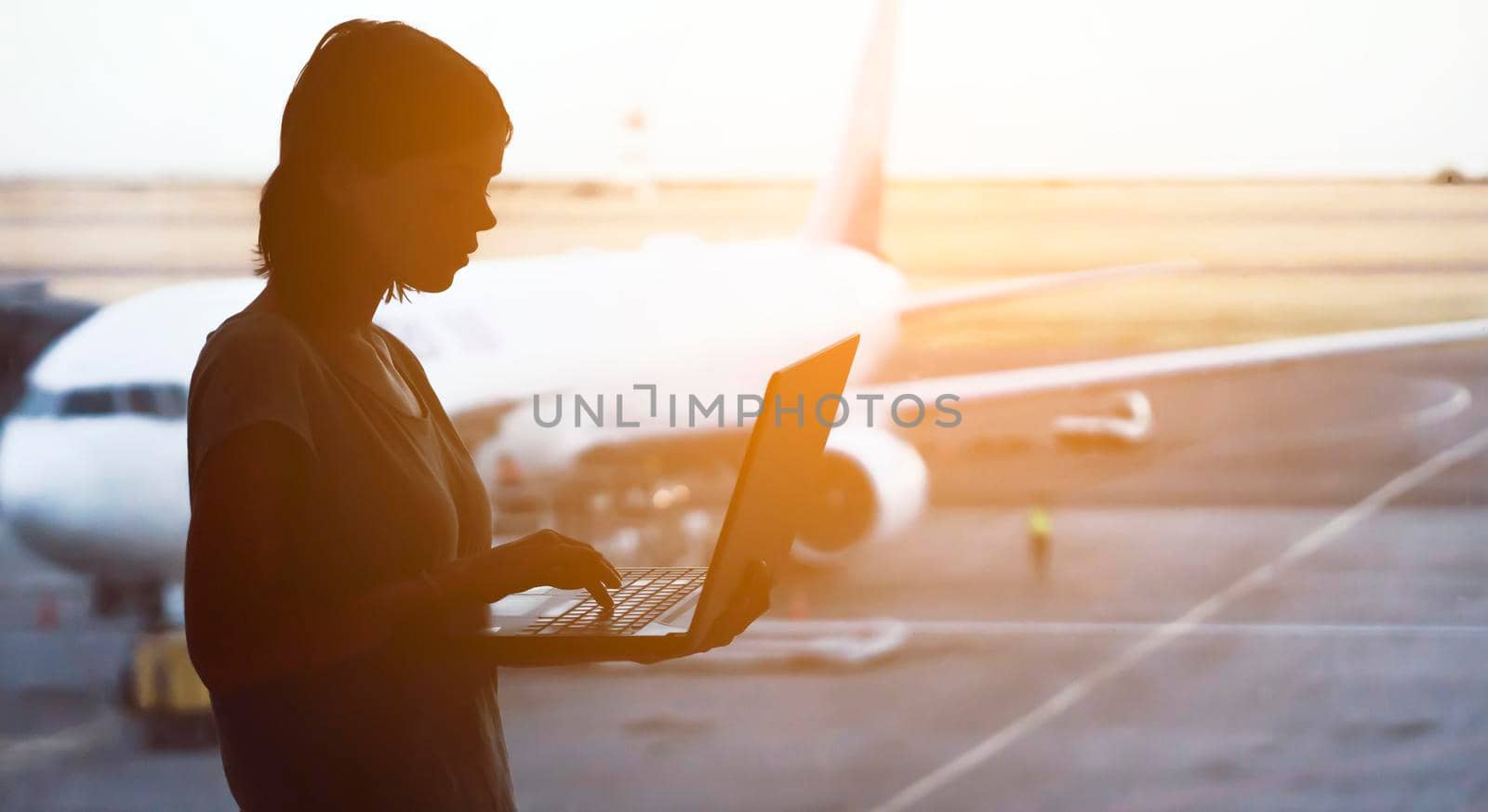 A young girl works on a laptop at the airport while she waits to board a plane. A woman buys tickets, studies and communicates via the Internet, the airport in the background.