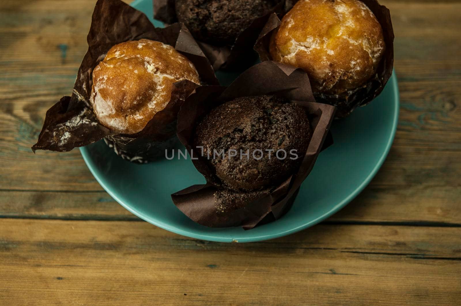 Homemade chocolate and vanilla cupcakes lie on ceramic plate on a wooden table, sprinkled with powdered sugar. Breakfast
