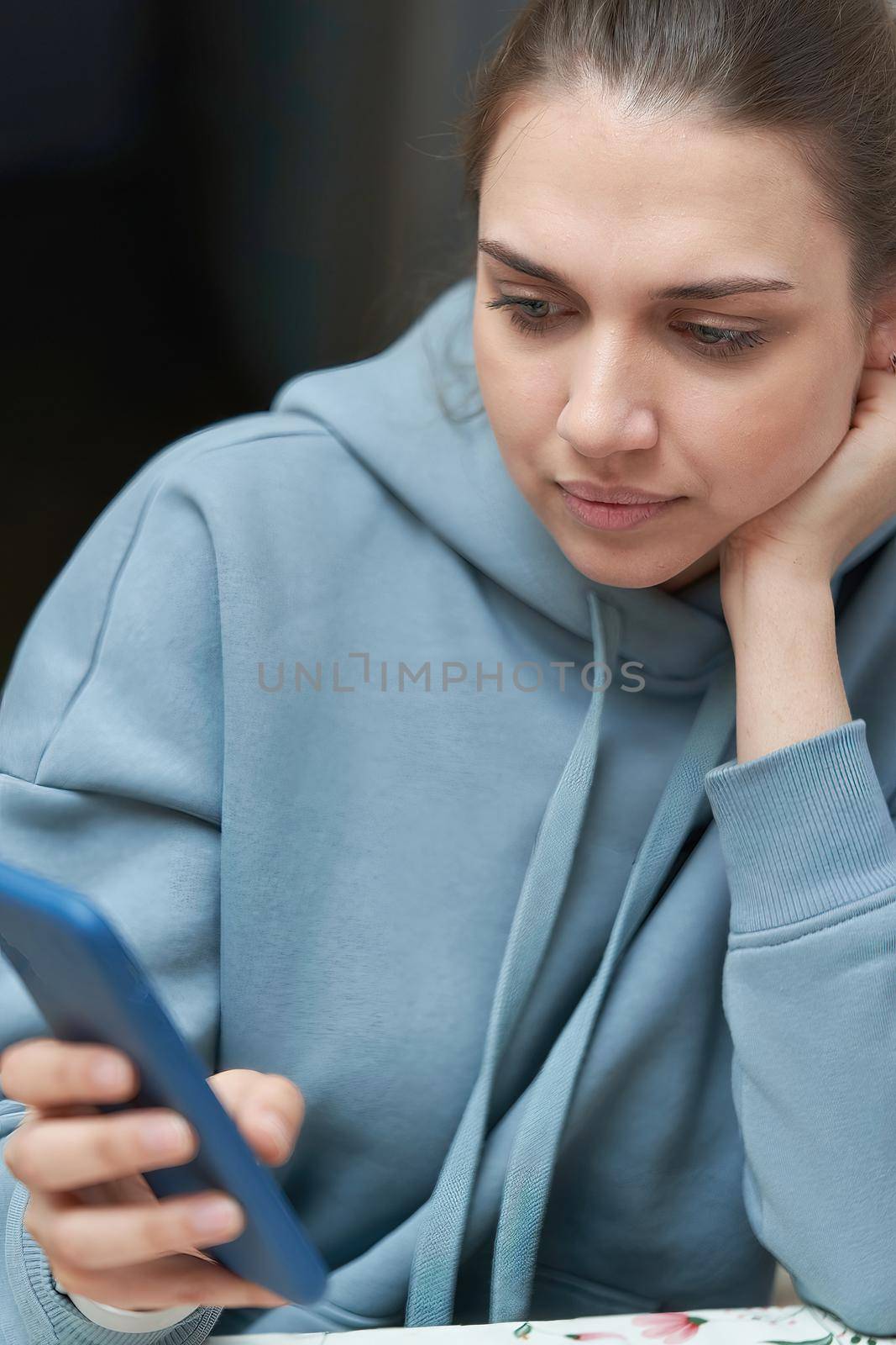 A beautiful brunette with long hair combed back looks into her smartphone. Vertical frame