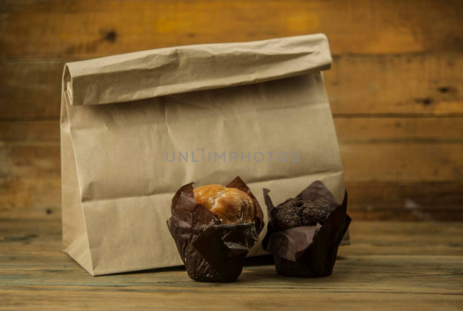 Homemade chocolate and vanilla cupcakes with paper lunch bag on a wooden table, sprinkled with powdered sugar. by inxti