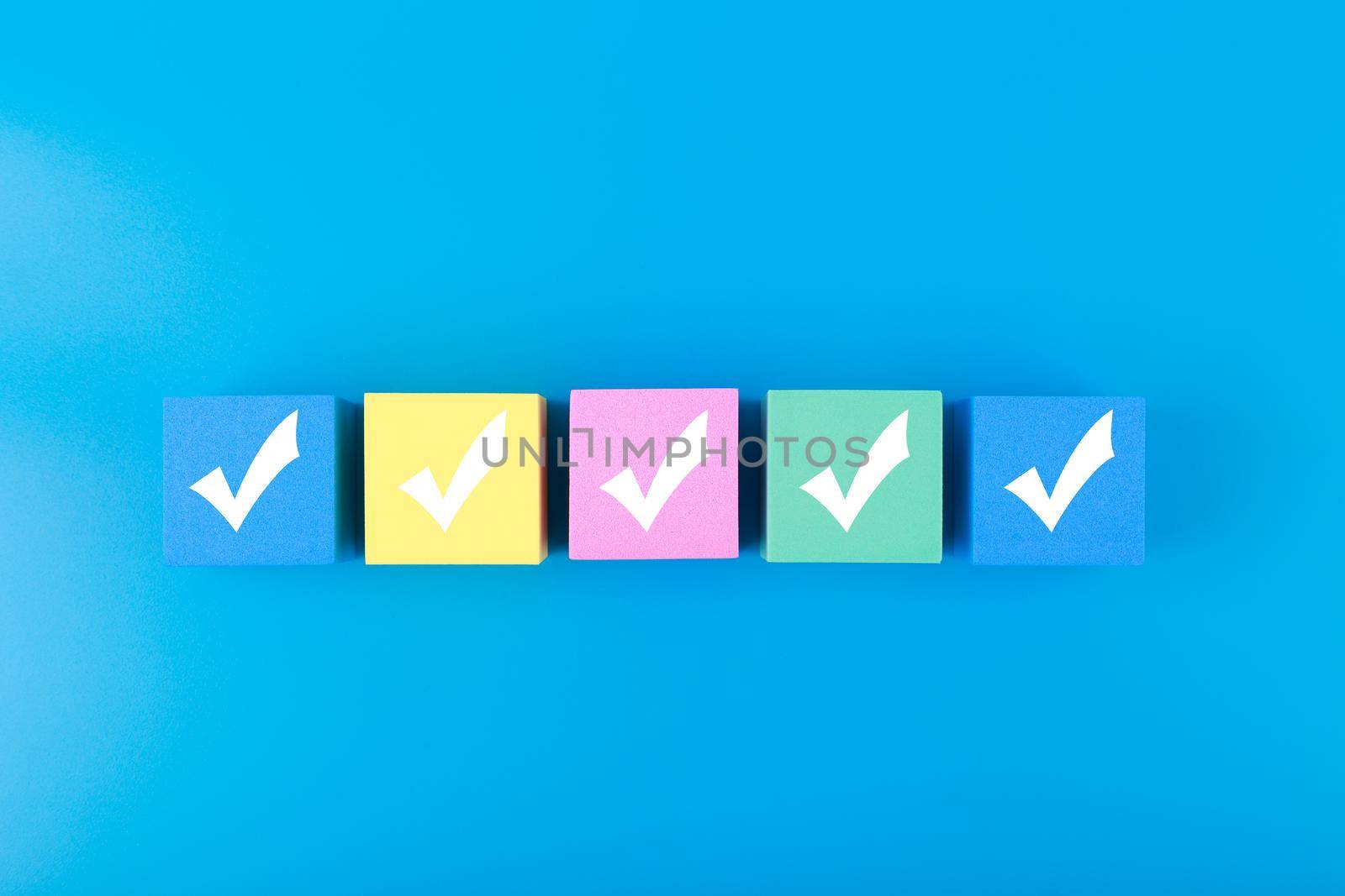 Five checkmarks on multicolored cubes in a row on blue background with copy space. Concept of questionary, checklist, to do list, planning, business or verification. Modern minimal composition