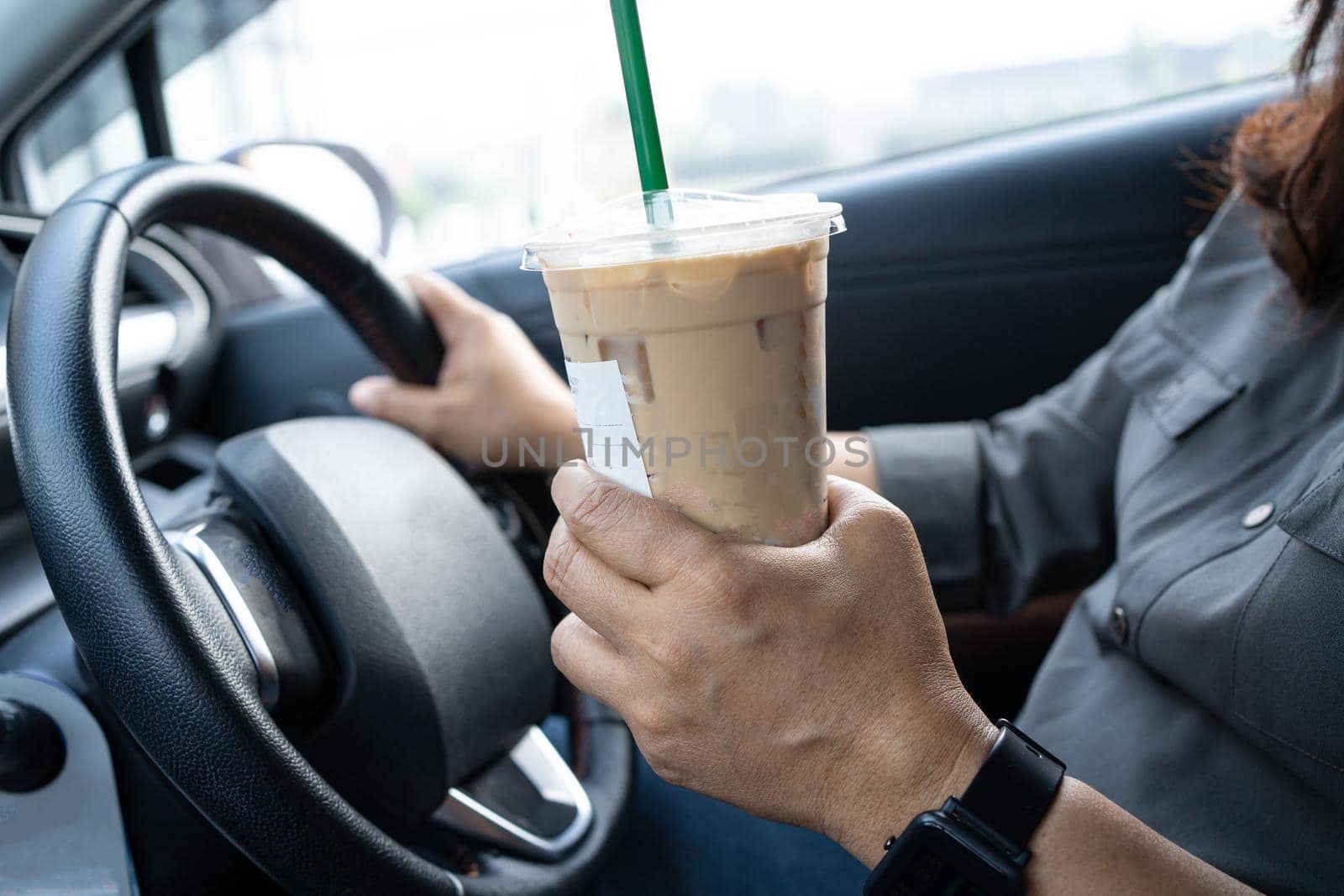 Asian lady holding ice coffee in car dangerous and risk an accident.