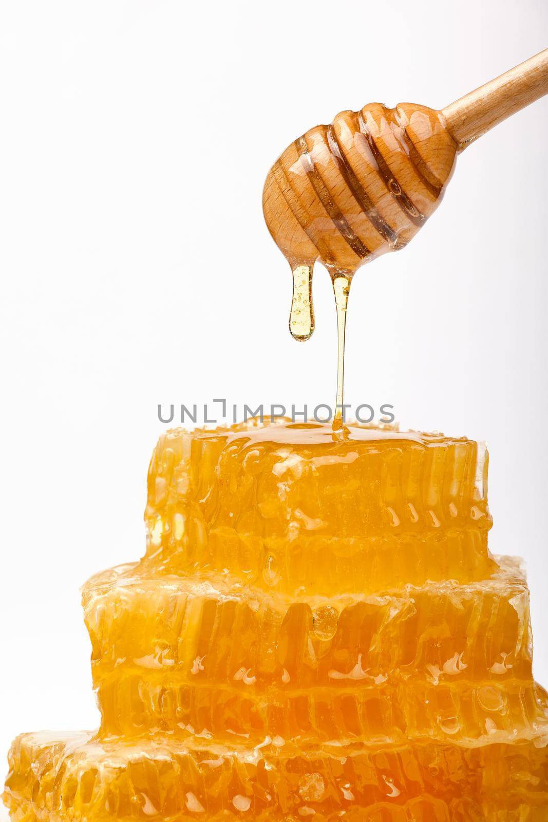 Close up stack of several fresh cut golden comb honey slices and natural wooden dipper, isolated on white background, low angle, side view