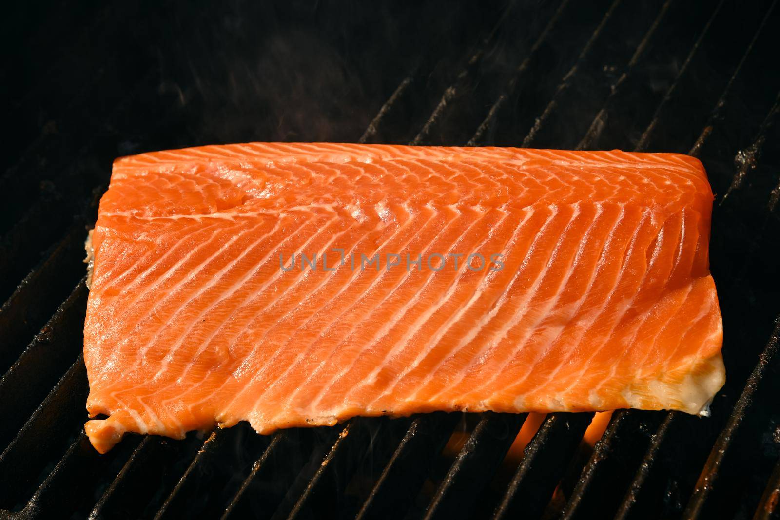 Close up searing and smoking salmon fish fillet on open fire outdoor grill with cast iron metal grate, high angle view