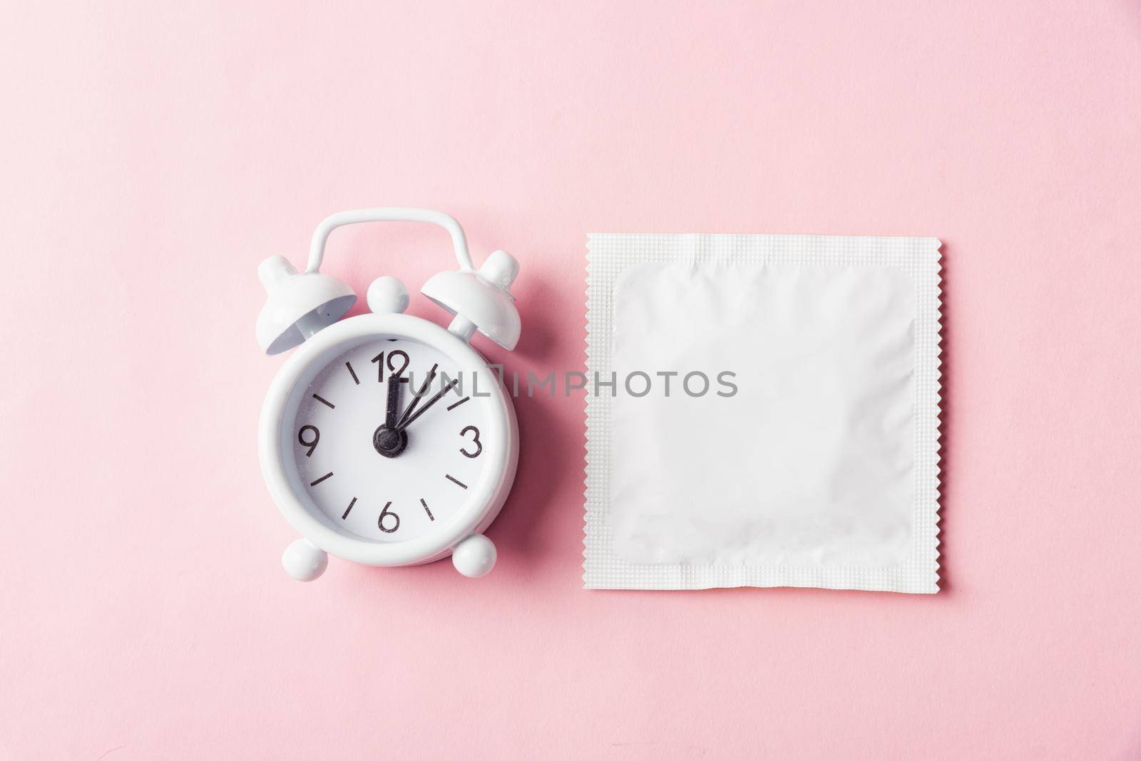 World sexual health or Aids day, condom in wrapper pack and Alarm clock birth control, studio shot isolated on a pink background, Safe sex and reproductive health concept