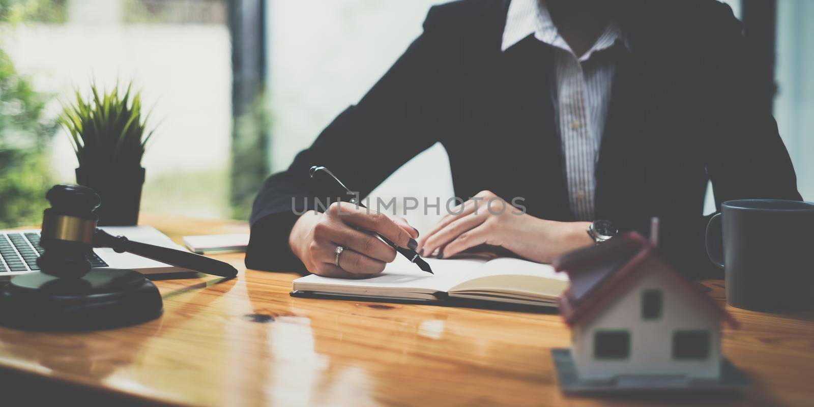 Business woman or legal advisor writting in book on wooden desk in office. Law, legal services, advice,Judge auction and real estate concept. by itchaznong