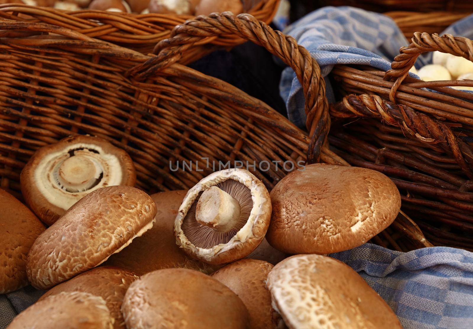 Close up mature brown portobello edible mushrooms (Agaricus bisporus) in wicker wooden basket at retail display, high angle view