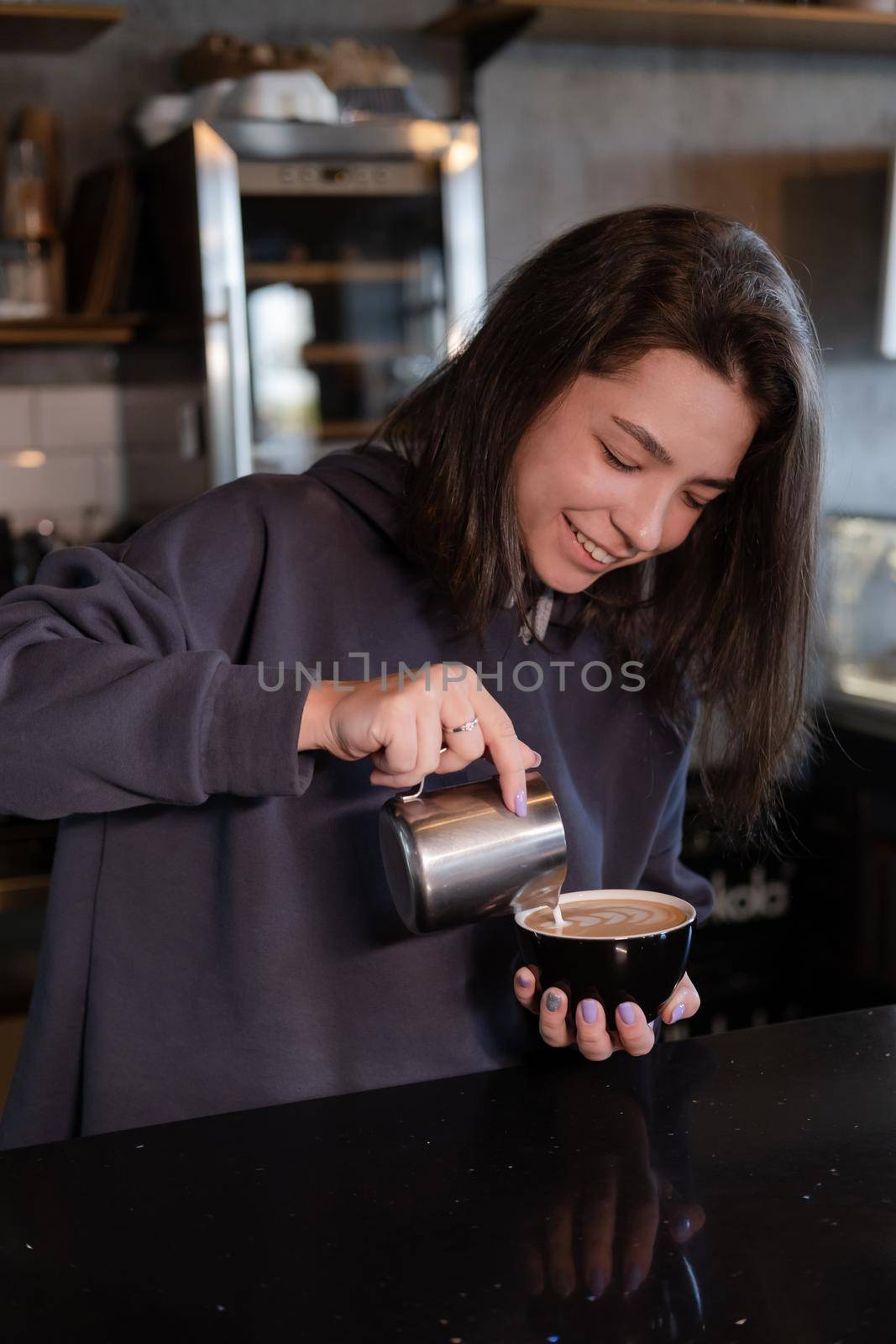 cute girl makes latte in coffee shop. Barista making coffee. Draws a drawing with milk on drink - cappuccino by oliavesna