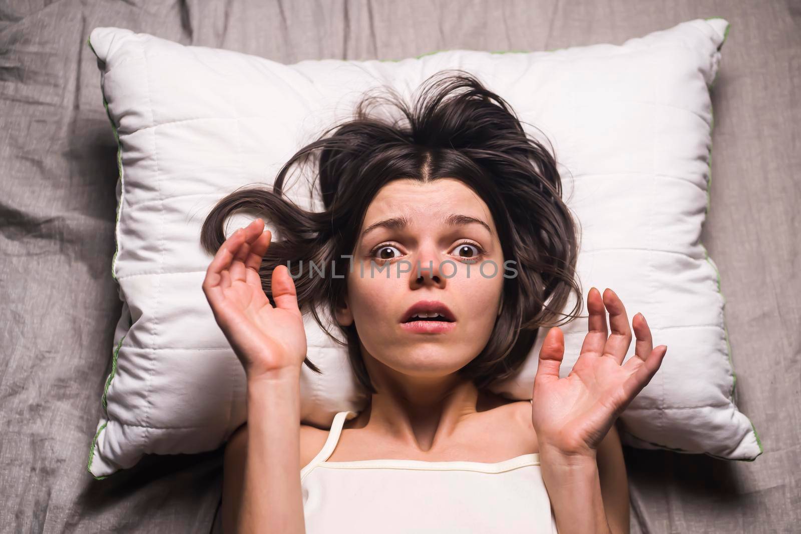 Young girl with a frightened expression wakes up from a nightmare in bed. Woman had a terrible unpleasant dream, she is experiencing a panic attack. Life stress, mental health problems and insomnia.