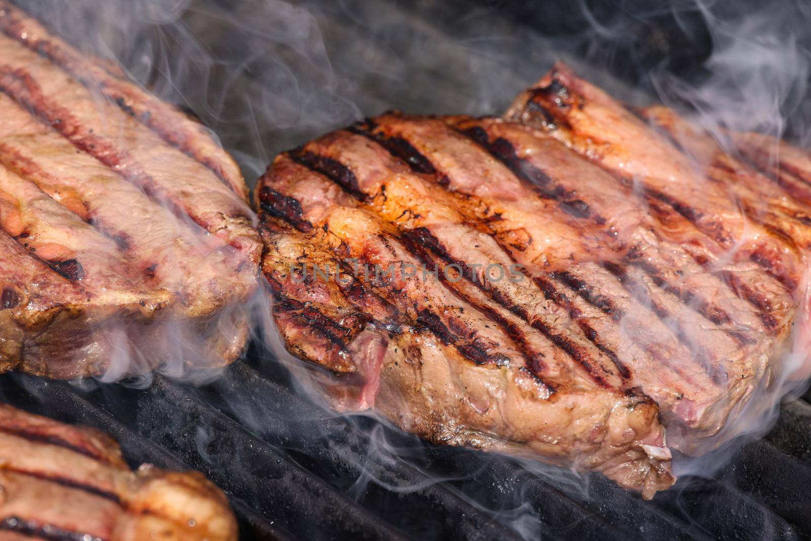 Close up searing and smoking ribeye beef steaks on open fire outdoor grill with cast iron metal grate, high angle view