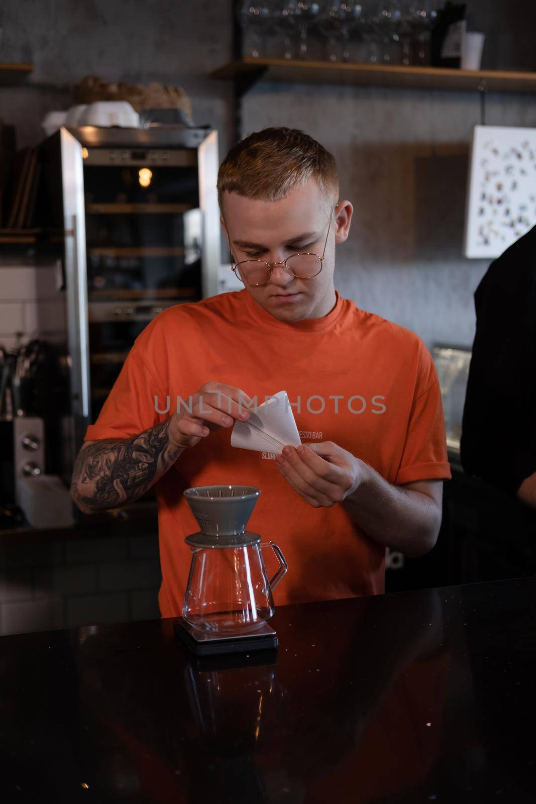 blonde guy in orange t-shirt preparing Alternative coffee brewing: chemex in modern loft coffee shop by oliavesna