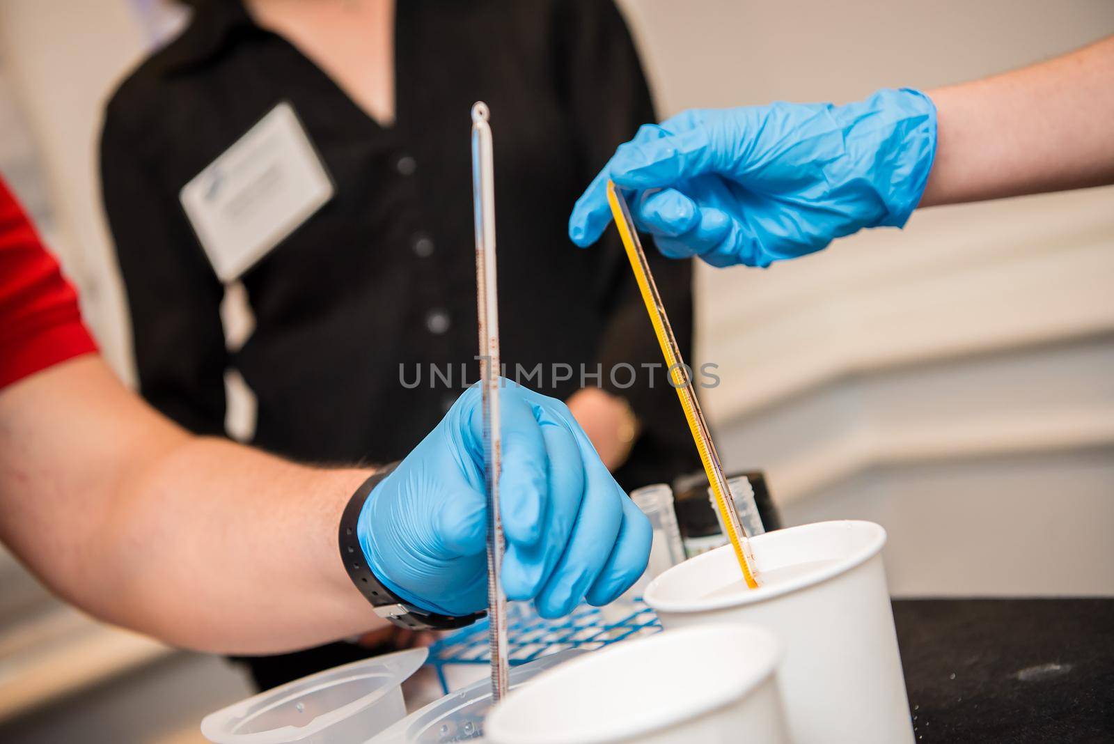 Up close view of young scientists wearing blue latex gloves stirring in a cup within a classroom setting post-covid.