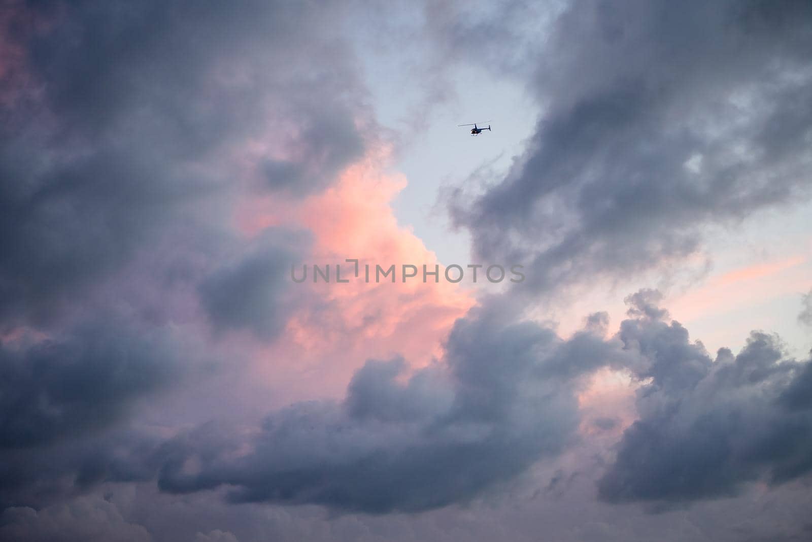 Heavenly view of pastel pink and purple clouds with single object helicopter flying into the abyss. Artistic view of sky
