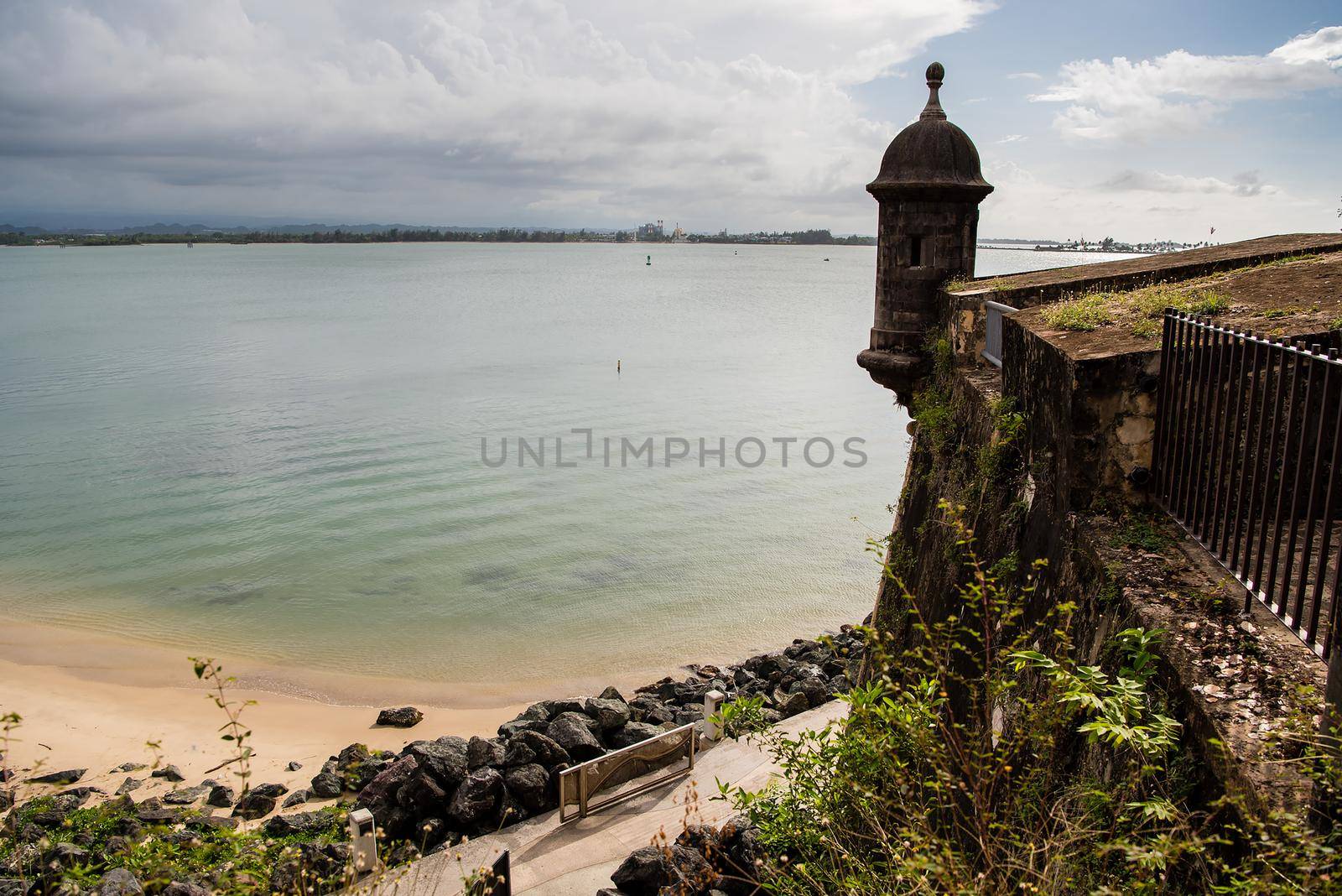 View of beach and castle tower in San Juan, Puerto Rico with clear waters and rocky beach. by jyurinko