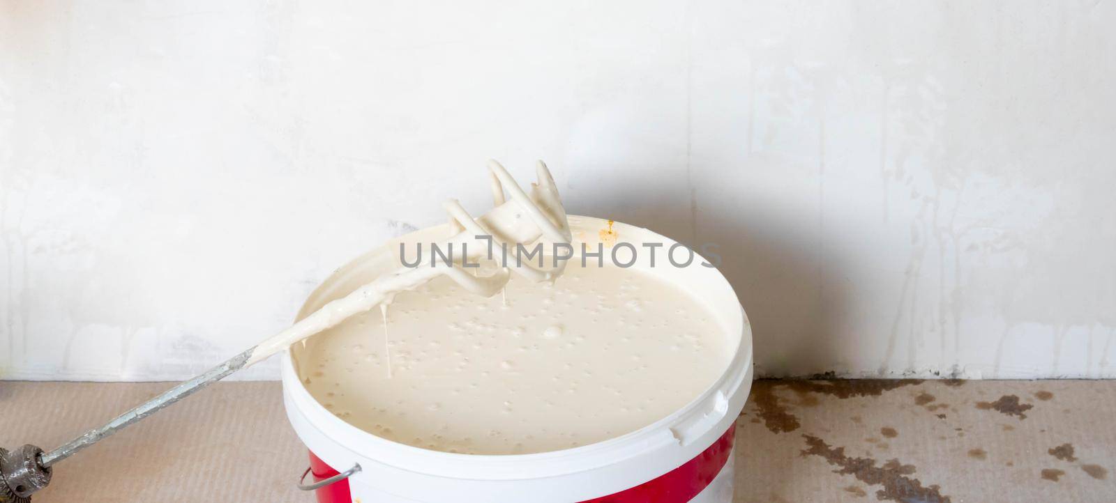 White paint in a bucket with a mixer on the floor. A bucket of white paint in the room. The concept of home improvement.
