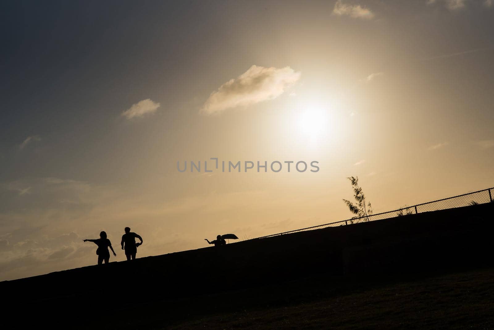 Silhouette lifestyle image of two people standing together with one pointing their finger up during sunset in San Juan, Puerto Rico. Warm tones