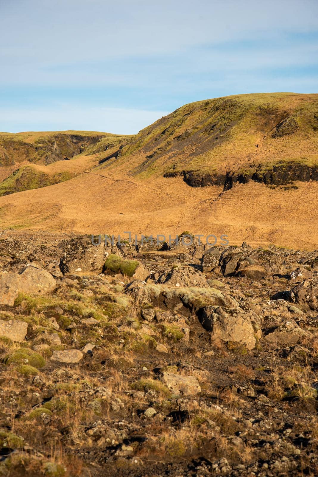 Icelandic topography with warm brown and orange tones and rocky texture with a blue sky by jyurinko