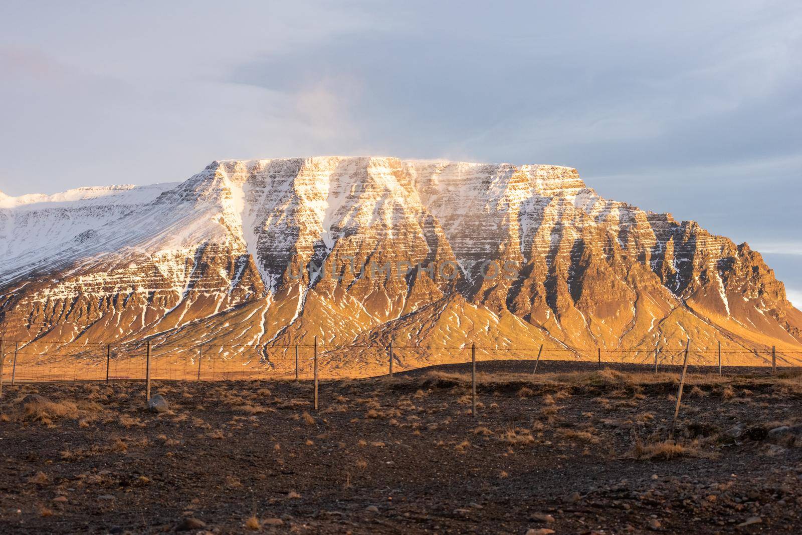 Golden brown snow capped mountain in Iceland with magical light casting down heavenly snow drive magical