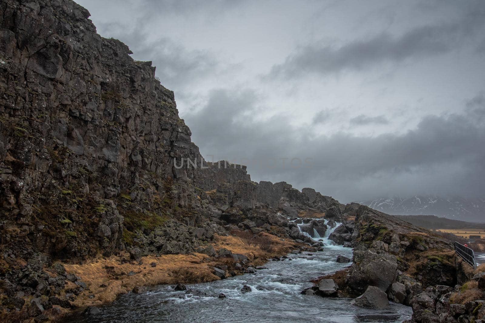 Rocky cliff with stormy skies and water rushing down a stream by jyurinko