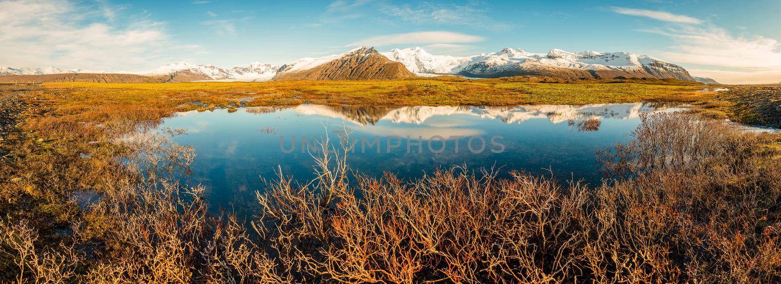 Icelandic mountain range with beautiful snowcapped mountains reflected into still water. Majestic panoramic view.