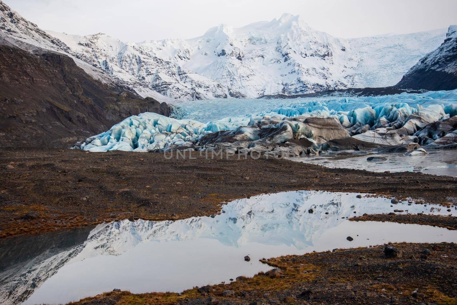 Bright blue Icelandic glacier with layers of glacier, volcanic ash, snow, and melted water with gorgeous reflection.