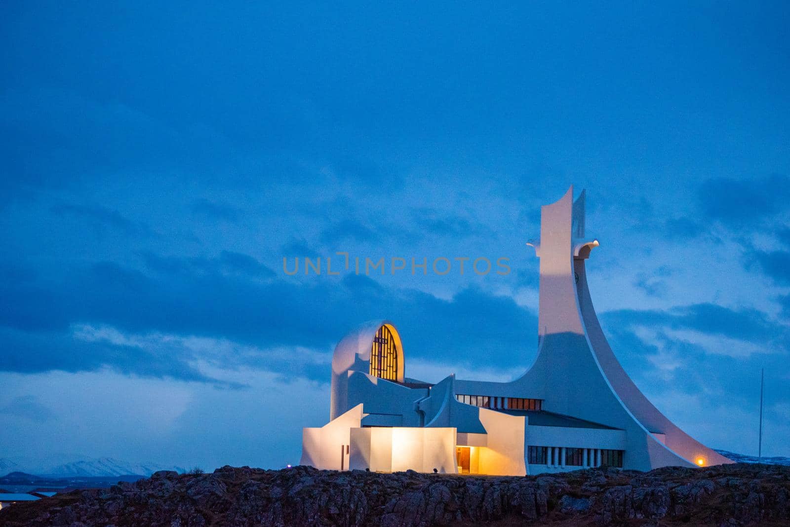 Uniquely shaped geometric church building with yellow glowing interior lights and a pretty blue sky backdrop